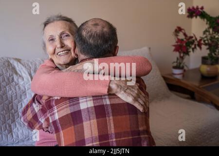 Donna anziana felice che abbraccia l'uomo maturo a casa Foto Stock