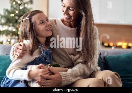 Felice madre che abbraccia la figlia seduta in soggiorno Foto Stock