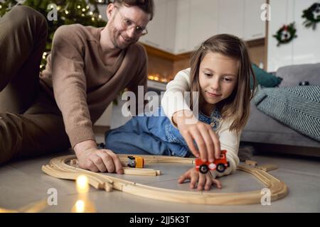 Uomo e figlia sorridenti che giocano con il treno in miniatura a casa Foto Stock