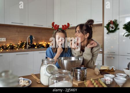 Donna felice con figlia degustazione biscotto glassando in cucina Foto Stock