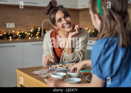 Donna felice con figlia che decora biscotti di pan di zenzero a casa Foto Stock