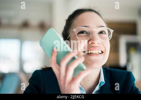 Donna d'affari sorridente che invia messaggi vocali tramite smartphone Foto Stock