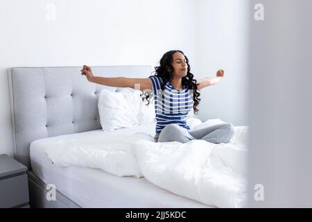Giovane donna che si sveglia e si allunga a letto a casa Foto Stock