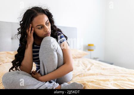 Donna preoccupata seduta con la testa nelle mani a casa Foto Stock