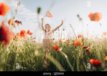 Ragazza felice inseguimento farfalle in campo papavero Foto Stock