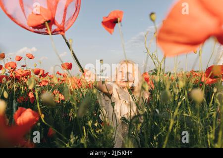 Ragazza giocosa che gioca con la rete rossa della farfalla in campo di papavero Foto Stock