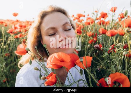 Donna sorridente con gli occhi chiusi seduto in mezzo a fiori rossi in campo Foto Stock