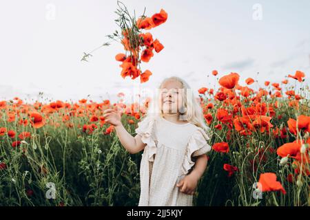 Ragazza giocosa che lancia il fiore in piedi nel campo di papavero Foto Stock