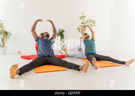 Le coppie multirazziali che praticano lo stretching esercitano insieme nello studio yoga Foto Stock