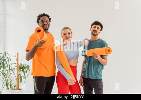 Uomini e donne sorridenti che tengono stuoie da ginnastica in studio yoga Foto Stock