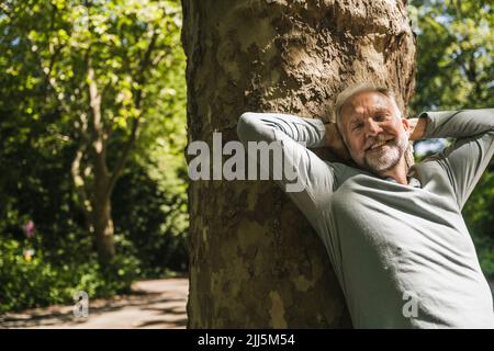 Uomo felice con gli occhi chiusi appoggiandosi sul tronco dell'albero Foto Stock