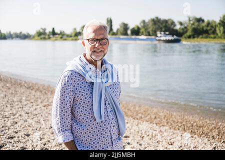 Uomo anziano sorridente che indossa occhiali in piedi sul lungofiume Foto Stock