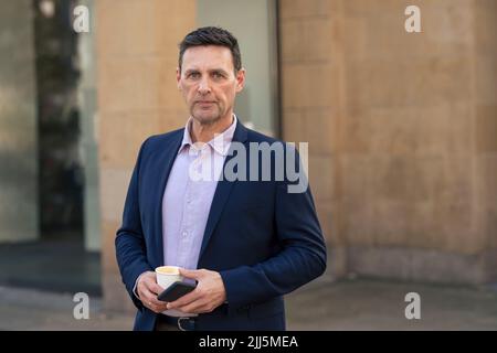 Uomo d'affari sicuro che tiene la tazza usa e getta e lo smartphone Foto Stock