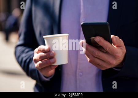 Mani di uomo d'affari che tengono la tazza usa e getta e lo smartphone Foto Stock