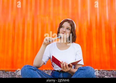 Ragazza pensierosa adolescente con il taccuino seduto davanti al contenitore arancione del carico Foto Stock