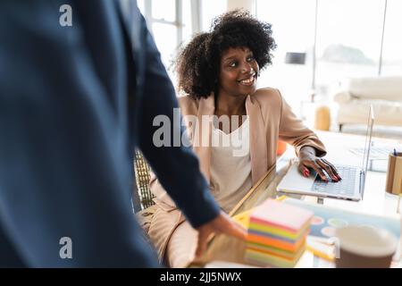 Donna d'affari sorridente con un computer portatile sul tavolo seduto in ufficio Foto Stock