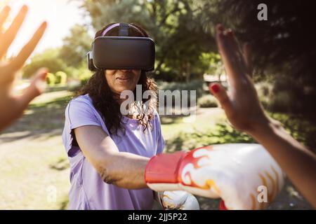 Sorridente ragazza pugilato con simulatore di realtà virtuale da figlia nel parco Foto Stock