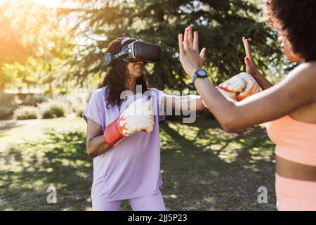 Donna anziana con occhiali di protezione per la realtà virtuale che si inscatolano con la figlia nel parco Foto Stock