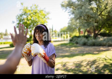 Donna anziana che pratica boxe con la figlia nel parco pubblico Foto Stock