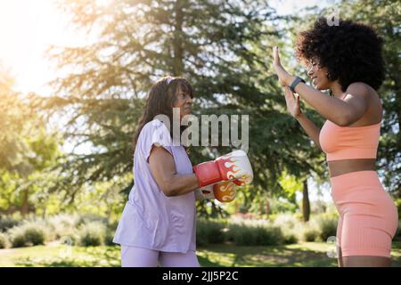 Donna anziana con guanti da boxe che pratica con la figlia nel parco Foto Stock