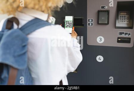 Donna che scansiona il codice QR sul distributore automatico di biglietti Foto Stock