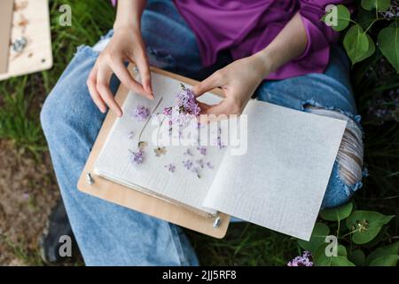 Donna che tiene fiori lilla seduta con libro Foto Stock