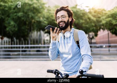 Uomo sorridente che indossa le cuffie wireless e parla con il telefono con vivavoce Foto Stock