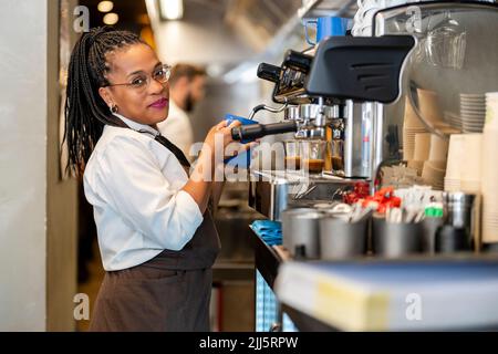 Barista sorridente che utilizza la macchina per il caffè nella cucina del ristorante Foto Stock