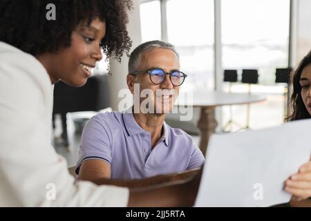 Uomo d'affari sorridente maturo che discute documento con le donne d'affari Foto Stock