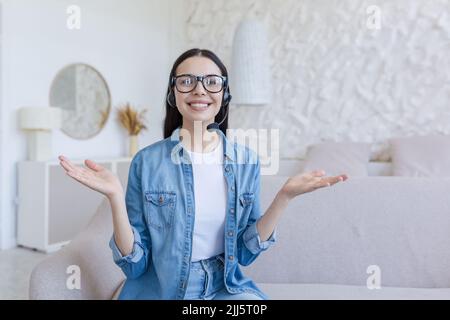 Donna felice e di successo che lavora da remoto a casa, guarda la webcam e sorride, utilizzando le cuffie per le videochiamate Foto Stock