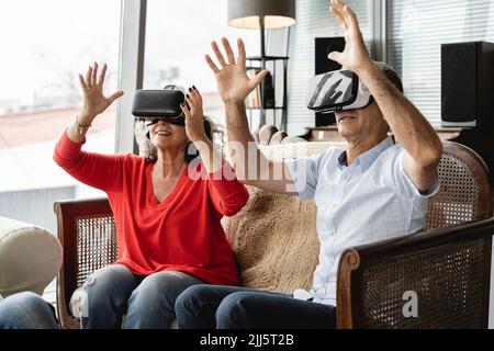 Colleghi di affari felici che indossano il simulatore di realtà virtuale seduto sul divano gesturing in ufficio Foto Stock