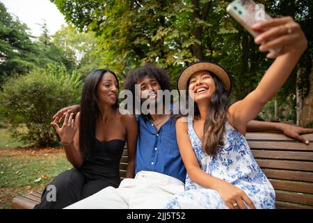 Tre amici del parco prendono un selfie e sorridono felicemente, gente di etnie differenti insieme Foto Stock