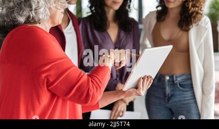 Donna d'affari anziana che parla di PC tablet con i colleghi Foto Stock