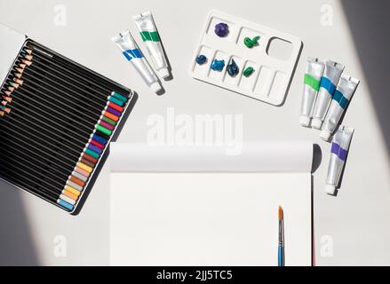 Studio di attrezzature d'arte e artigianato tra cui matite colorate, carta da disegno bianca, tubi di vernice ad olio, tavolozza di artisti e singolo pennello Foto Stock
