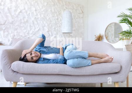 Sola e malata bella donna sola a casa, sdraiata sul divano, tenuta mano a testa, emicrania e forte mal di testa Foto Stock