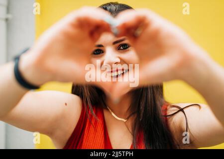 Donna sorridente che forma il cuore con le mani Foto Stock