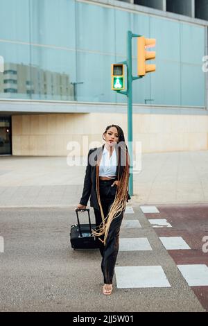 Giovane donna d'affari con valigia che attraversa la strada Foto Stock