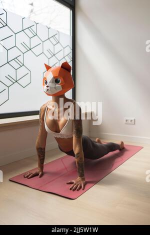 Donna con maschera animale che pratica yoga sul tappeto in studio Foto Stock