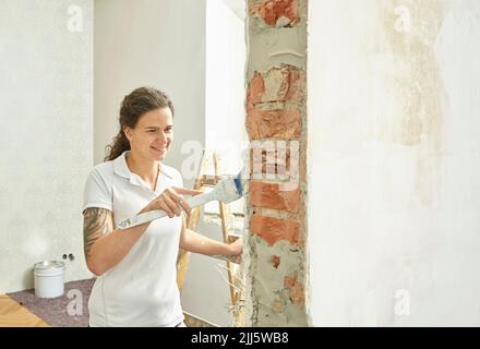 Pittore sorridente che fa la vernice finale con pennello in appartamento Foto Stock