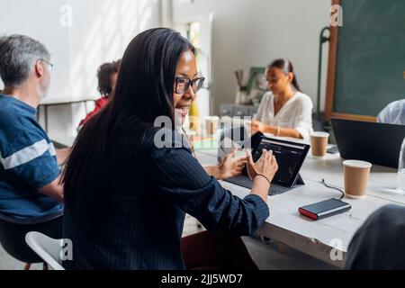 Donna d'affari con occhiali che parlano con il collega alla scrivania in ufficio Foto Stock