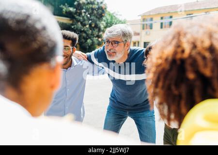 Uomo d'affari maturo con le braccia intorno ai colleghi in giornata di sole Foto Stock