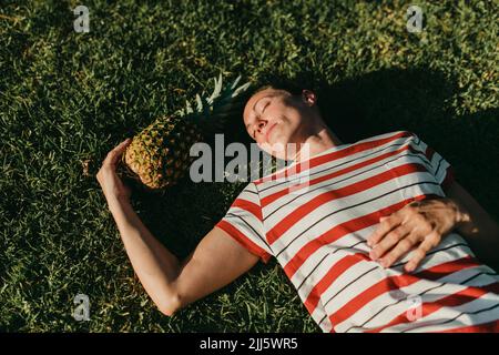 Donna rilassante da ananas sull'erba nel parco Foto Stock
