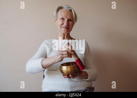 Donna anziana felice con cantare ciotola di fronte al muro Foto Stock