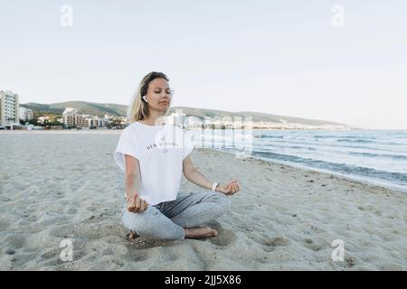 Donna sorridente con occhi chiusi meditando in spiaggia Foto Stock