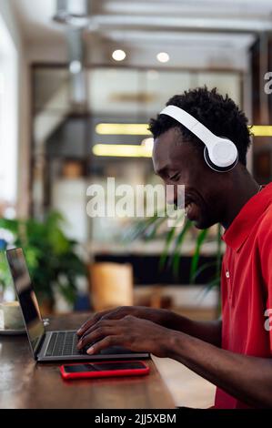 Uomo sorridente che indossa cuffie wireless utilizzando un computer portatile Foto Stock