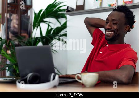 Uomo sorridente con mano dietro la testa seduto in caffetteria Foto Stock