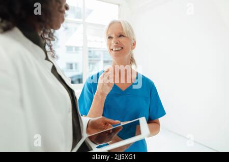 Infermiera sorridente che parla con il medico che tiene il tablet PC Foto Stock