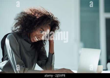 Donna d'affari felice con mano in capelli utilizzando il portatile in ufficio Foto Stock
