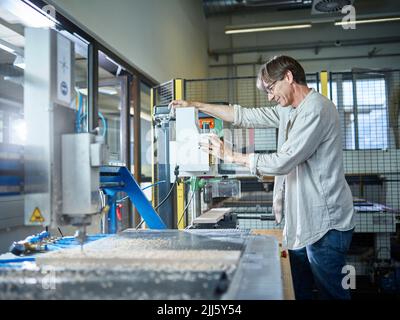 Uomo maturo che lavora su macchine per legno in fabbrica Foto Stock