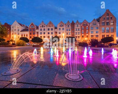 Polonia, Voivodeship Warmian-Masurian, Elblag, fontana colorata nella piazza della città vecchia con rose sullo sfondo Foto Stock
